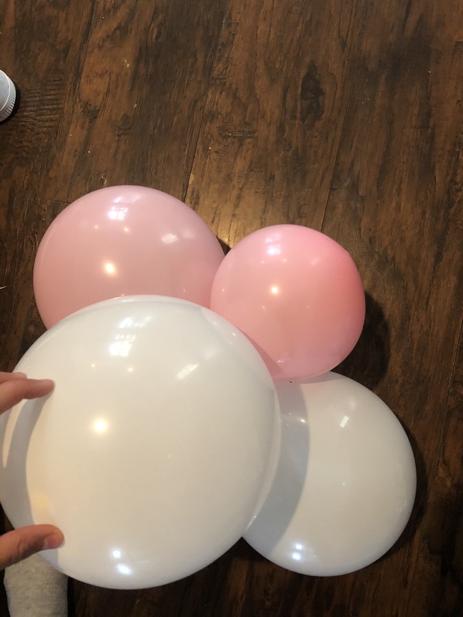 Four balloons are shown in a clump like grapes. They are resting on the floor. Three balloons appear to be making the base on which the fourth larger balloon sits. A hand is visible holding the balloon clump steady. This caption may sound strange because honestly it is also unclear what exactly is going on in the image. Kara Steele