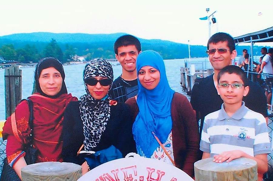A family picture from my family's visit to Lake George. We went there to celebrate my oldest sister's last birthday with us before she got married and moved away. A Pakistani family is standing by the dock in front of Lake George in New York. There are two sisters and their mother wearing hijab on the left, with two brothers behind them and the third brother who looks to be the youngest around 12, standing on the right. The older sister is wearing sun glasses and a leopard spotted hijab, while the younger sister has a light blue hijab. The father is the one taking the photo so he is not in the picture. Sameer Riaz